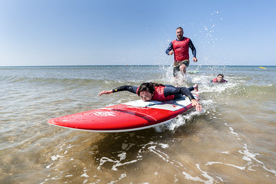 Surfeuse handisport qui glisse couchée suivi à pied de son pousseur